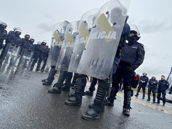 Na zdjęciu policjanci z uniesionymi tarczami z napisem policja. stoją w szeregu czteroosobowym. w tle inni policjanci