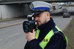 Zdjęcie przedstawia umundurowanego policjanta kontrolującego prędkość pojazdów