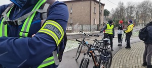 Zdjęcie przedstawia policjanta z odblaskową opaską z napisem &quot;Policja&quot; oraz innych uczestników wydarzenia