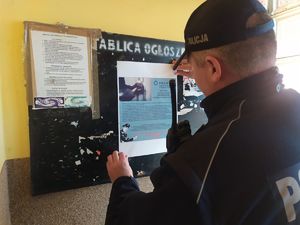 Zdjęcie przedstawia policjanta wieszającego plakat informacyjny na tablicy ogłoszeń