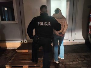 Zdjęcie przedstawia policjanta, który prowadzi zatrzymaną