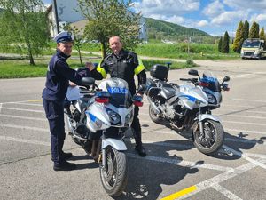 Zdjęcie przedstawia policjantów witających się przy motocyklach