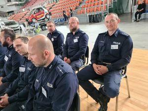 Zdjęcie przedstawia policjantów siedzących na hali sportowej