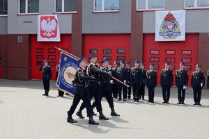 Zdjęcie przedstawia poczet sztandarowy na tle strażaków