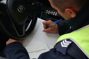 Zdjęcie przedstawia policjanta rozpisującego notatnik w radiowozie