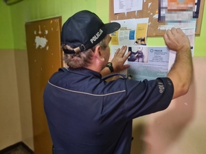 Zdjęcie przedstawia policjanta, który umieszcza plakat na tablicy ogłoszeń