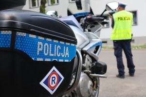 Zdjęcie przedstawia policyjny motocykl, w tle policjant