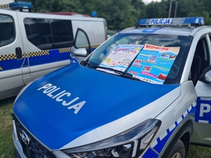 Zdjęcie przedstawia policyjny radiowóz, na którm naklejone są plakaty dotyczące bezpiecznych wakacji
