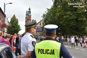 Zdjęcie policjanta oraz strażnika miejskiego na tle kościoła oraz pielgrzymów