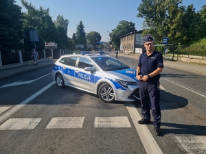 Zdjęcie przedstawia policjanta oraz policyjny radiowóz