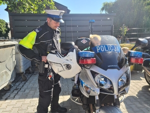 Zdjęcie przedstawia policjanta stojącego przy motocyklu