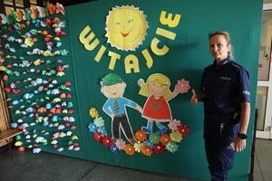 Zdjęcie przedstawia policjantkę stojącą przy tablicy z napisem witajcie
