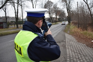 zdjęcie przedstawia funkcjonariusza kontrolującego prędkość przejeżdżającego samochodu