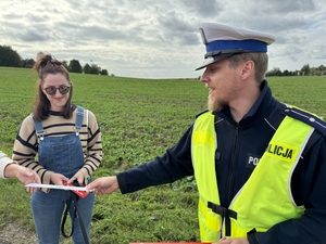 Zdjęcie przedstawia policjanta wręczającego odblask