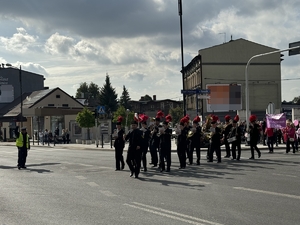 Zdjęcie przedstawia przemarsz uczestników Różowej Wstążki. Na czele idzie orkiestra