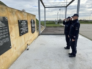 Zdjęcie przedstawia policjantów oddających honor przed pamiątkową tablicą