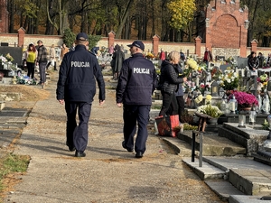 Zdjęcie przedstawia policjantów idących po cmentarzu