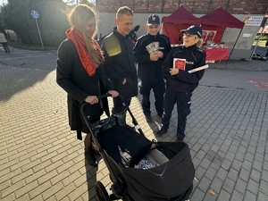 Zdjęcie przedstawia policjantów oraz kobietę, mężczyznę oraz wózek dziecięcy