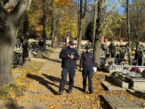 Zdjęcie przedstawia policjantów idących po cmentarzu