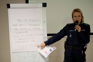 Zdjęcie przedstawia policjantkę wskazująca na kartkę papieru podczas prelekcji