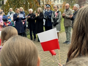 Zdjęcie przedstawia flagę trzymaną przez dzieci. W tle uczestnicy wydarzenia