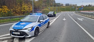 Zdjęcie przedstawia radiowóz oraz policjanta kontrolującego kierującego