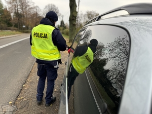 Zdjęcie przedstawia policjanta stojącego przy kontrolowanym samochodzie