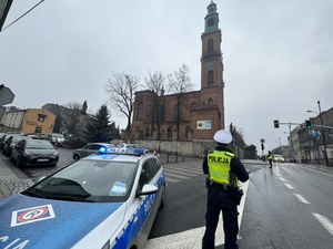 Zdjęcie przedstawia policjantów oraz radiowóz na tle kościoła