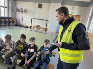 Zdjęcie przedstawia policjanta wręczającego dzieciom ulotki