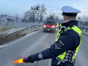 Zdjęcie przedstawia policjanta dającego latarką sygnał do zatrzymania się