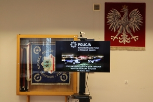 Zdjęcie przedstawia monitor, na którym wyświetlona jest informacja o odprawie rocznej w komendzie Policji w Piekarach Śląskich
