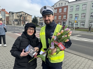 Zdjęcie przedstawia policjanta wręczającego kwiaty paniom.