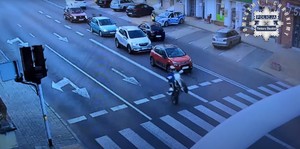 Zdjęcie motocyklisty jadącego na jednym kole po drodze. W tle patrol Policji