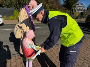 Zdjęcie przedstawia policjanta wręczającego przechodniom odblaskowe opaski