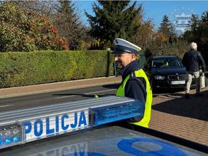 Zdjęcie przedstawia policjanta wręczającego przechodniom odblaskowe opaski