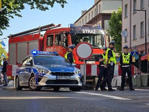 Zdjęcie policjantów stojących obok radiowozu i wozu strażackiego podczas zabezpieczenia pielgrzymki