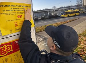 Zdjęcie dzielnicowego umieszczającego plakat na słupie ogłoszeniowym