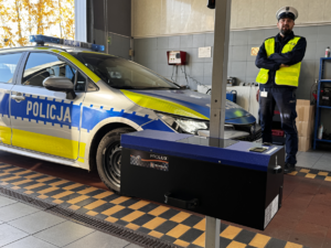 Zdjęcie policjanta stojącego przy radiowozie na stacji kontroli pojazdów