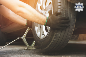 grafika przedstawia osobę wymieniającą koło w samochodzie