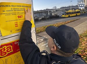 Policjant wieszający plakat z numerem infolinii