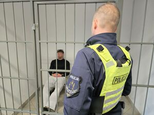 Policjant stoi przy pomieszczeniu dla osób zatrzymanych, w którym siedzi zatrzymany mężczyzna
